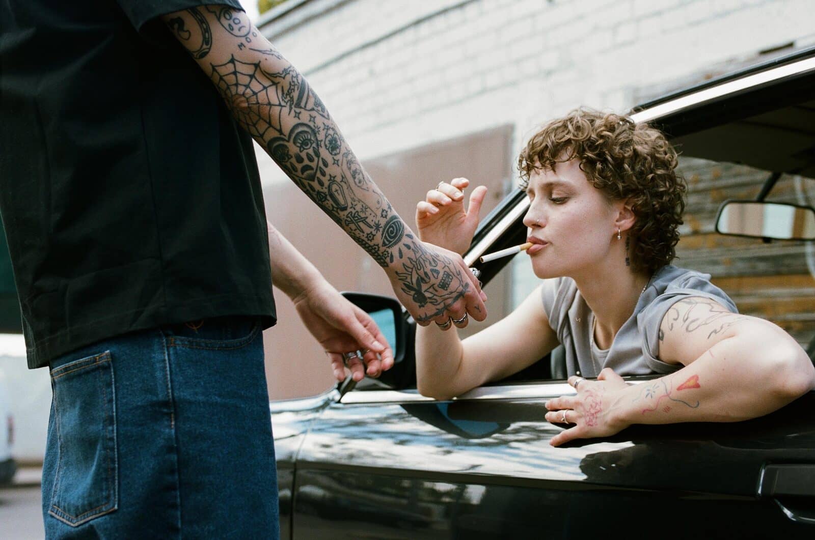 Cigaretė prisidegama pro automobilio langą – dvi rankos, liepsna, garbanos vasaros ore.